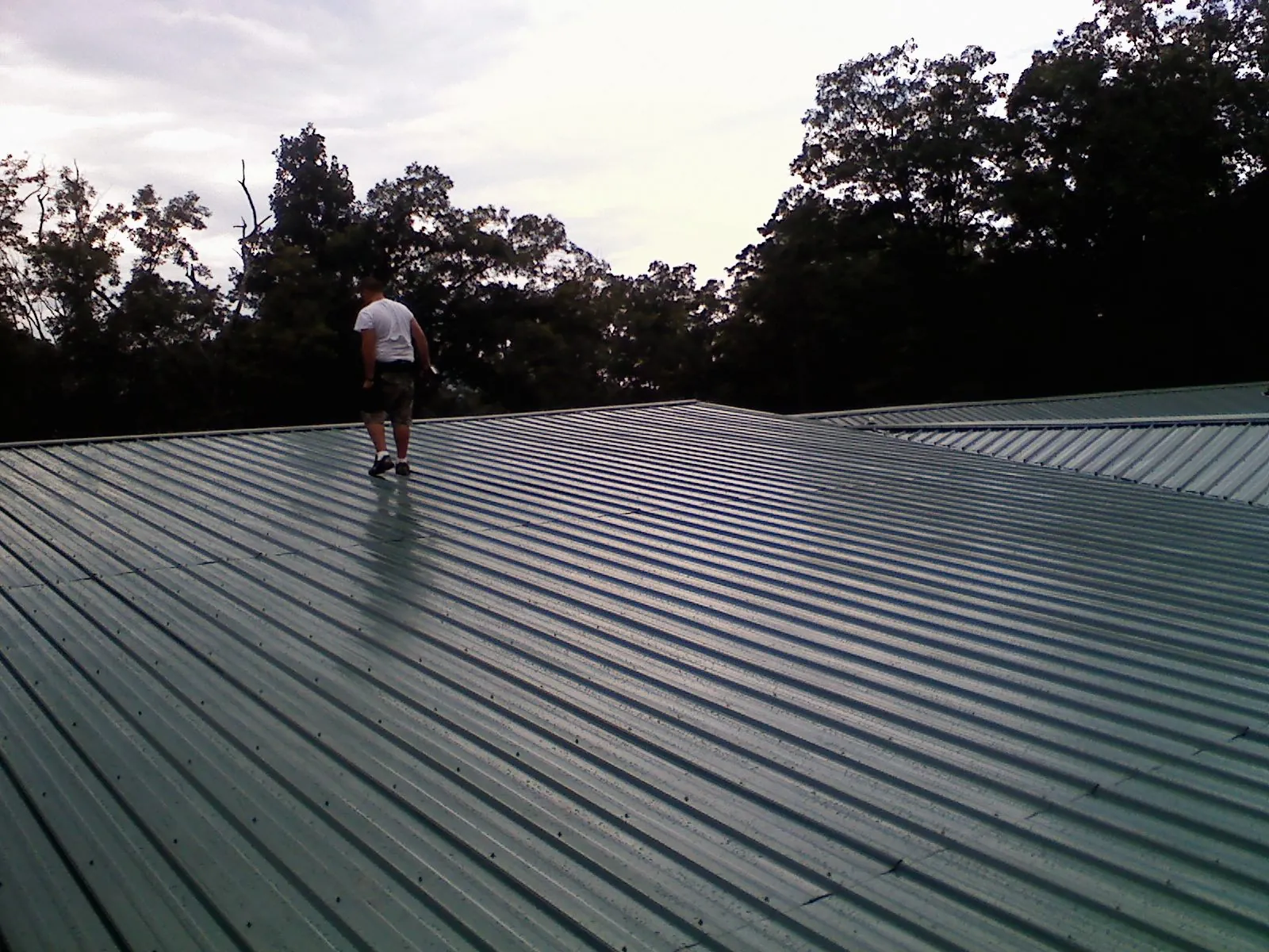 Roofer walking a wide expanse of new green metal roofing in Gilbert